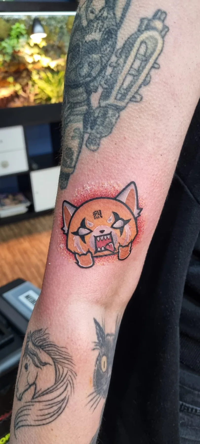 Colour cartoon tattoo of the angry red panda Aggretsuko on the forearm, among older tattoos, tattoo studio Vienna