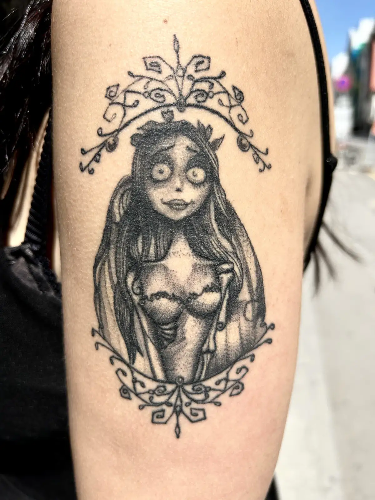 Dotwork tattoo of Emily from "Corpse Bride" in an ornate filigree frame on the upper arm, black and grey, Vienna