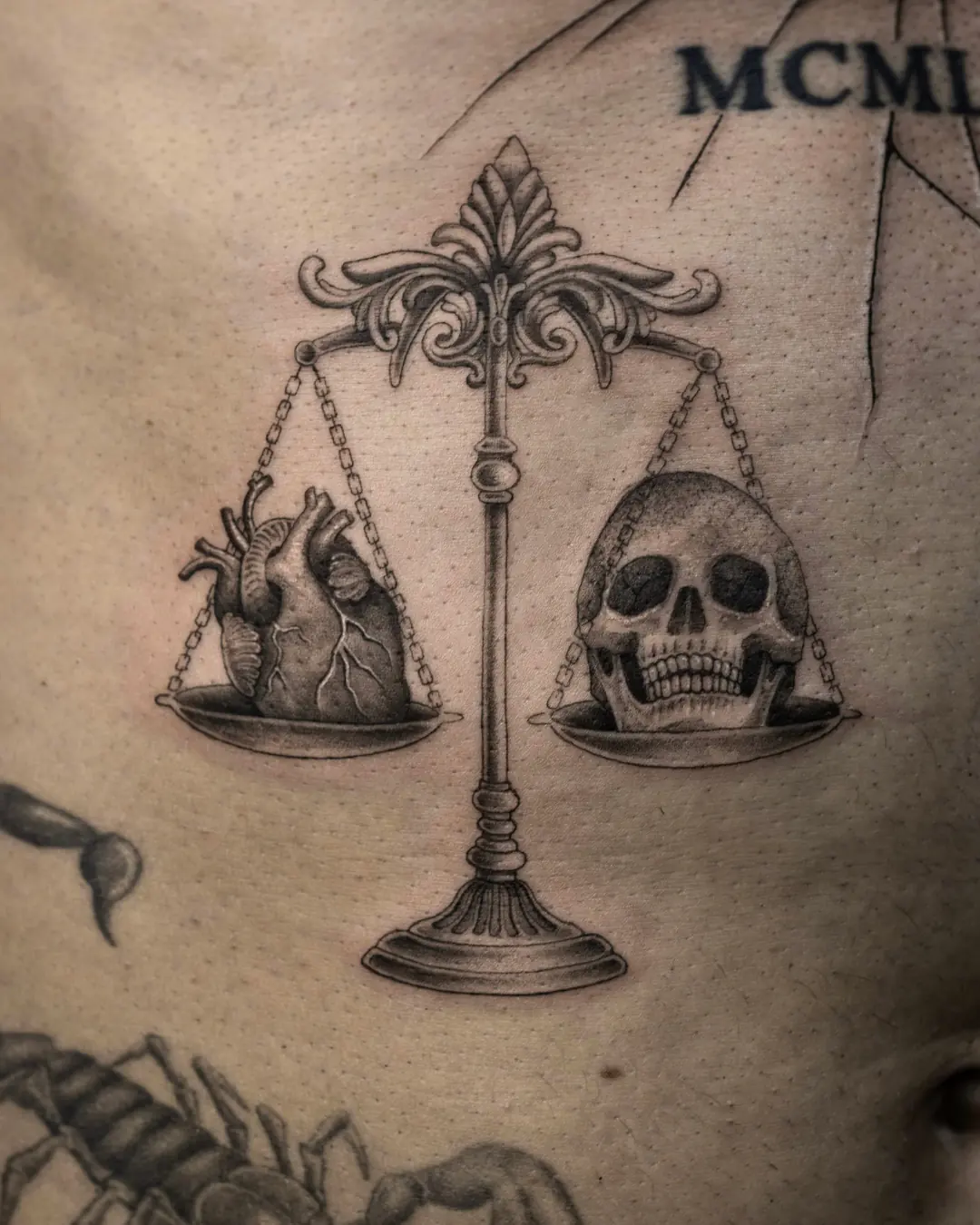 Fine line tattoo of an ornate scale holding an anatomical heart and a skull on the stomach, black and grey, Vienna