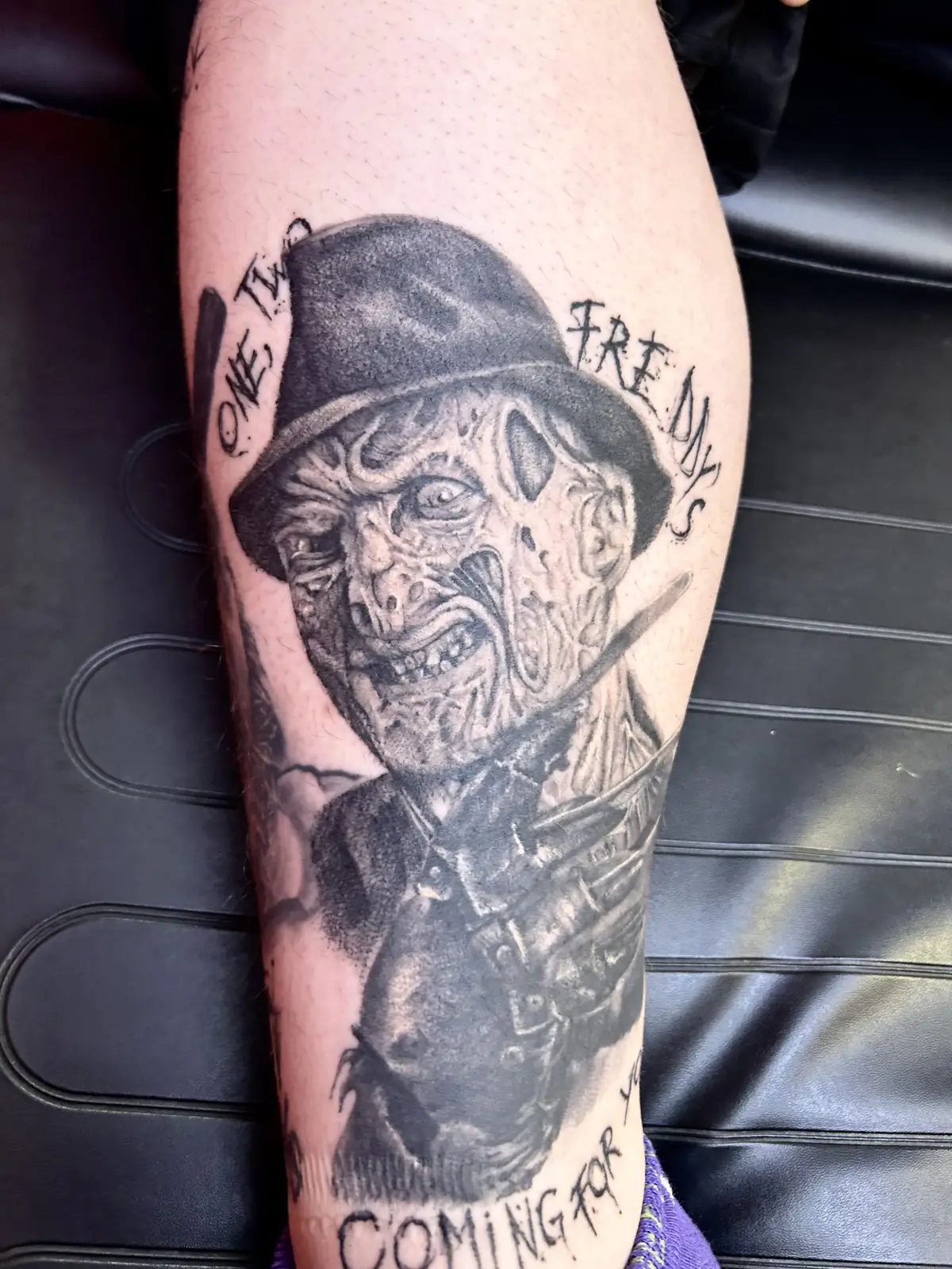 Realistic black and grey portrait tattoo of Freddy Krueger with his hat and bladed glove on the calf, with lettering, Vienna