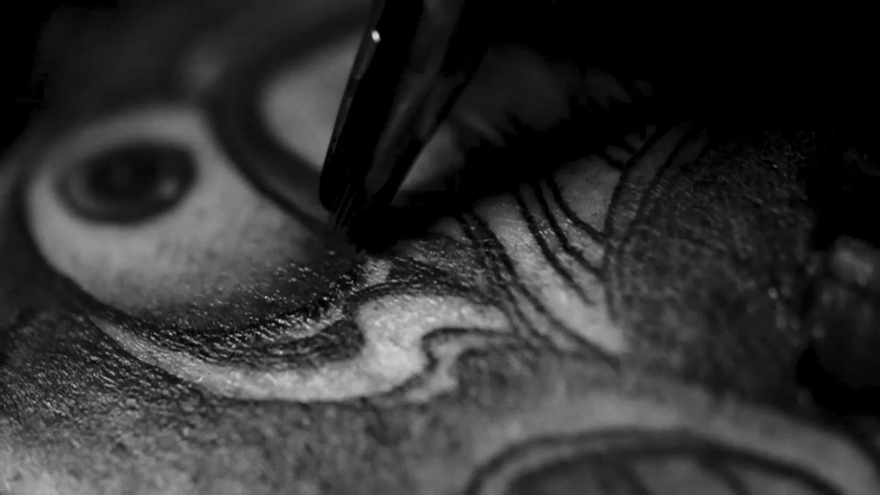 Close-up of a tattoo needle shading a black and grey tattoo with an eye and curved lines, tattoo studio Vienna