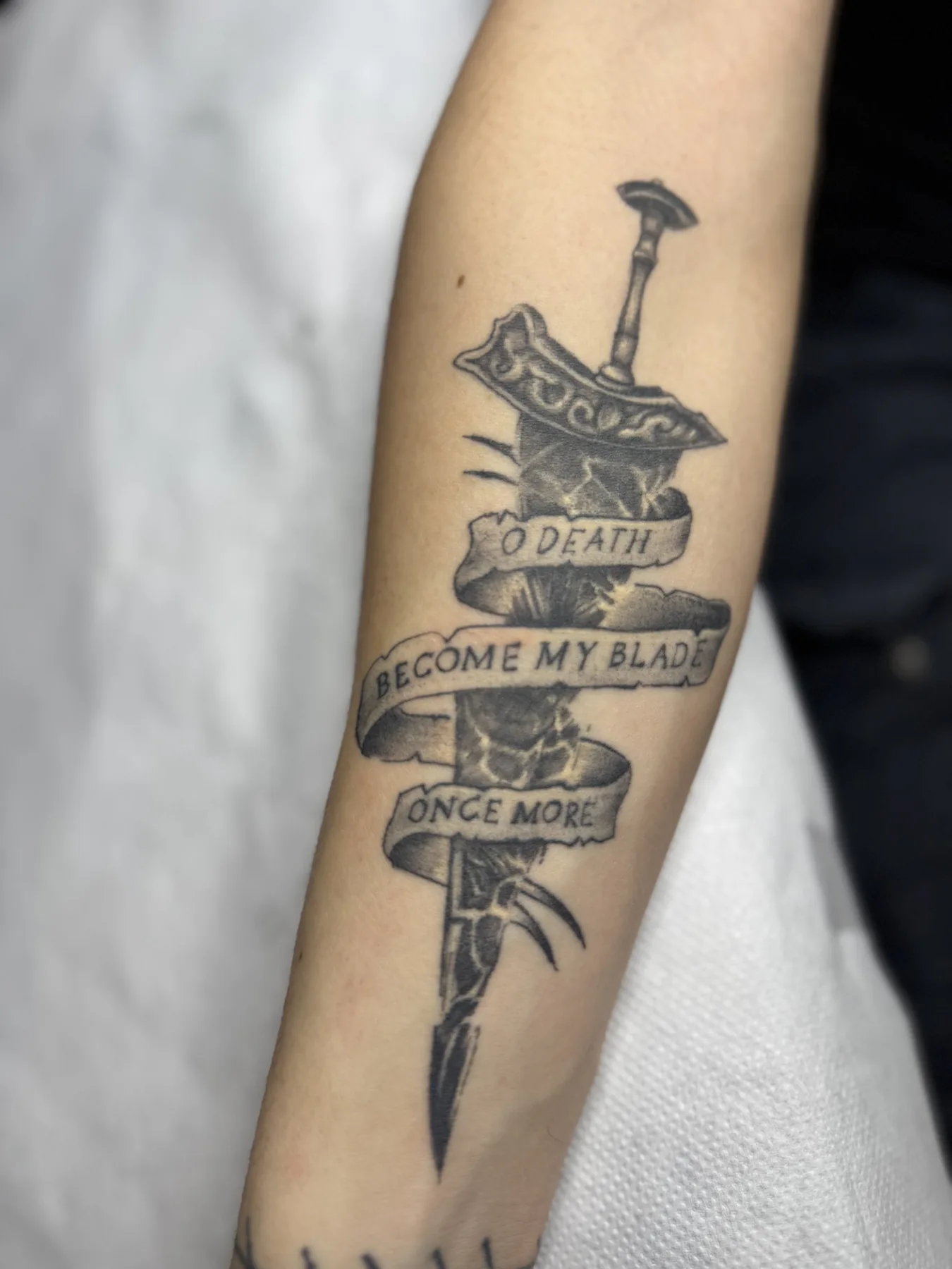 Sword with three lettered ribbons. Tattoo at Ink21 in Vienna.