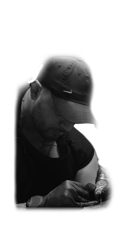 Tattoo artist Veso in a cap and black gloves working on a tattoo, black-and-white photo from the Vienna studio