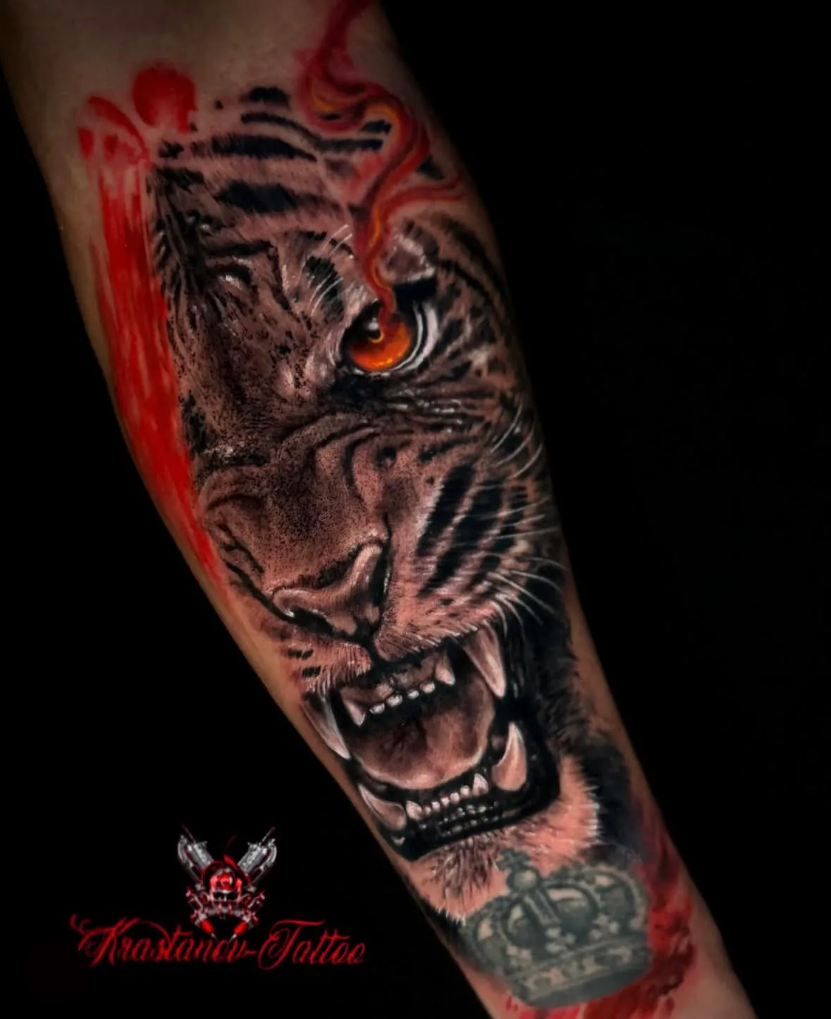 Realistic black and grey tiger tattoo on the forearm with an orange eye, a crown and red splashes, by Veso, Vienna
