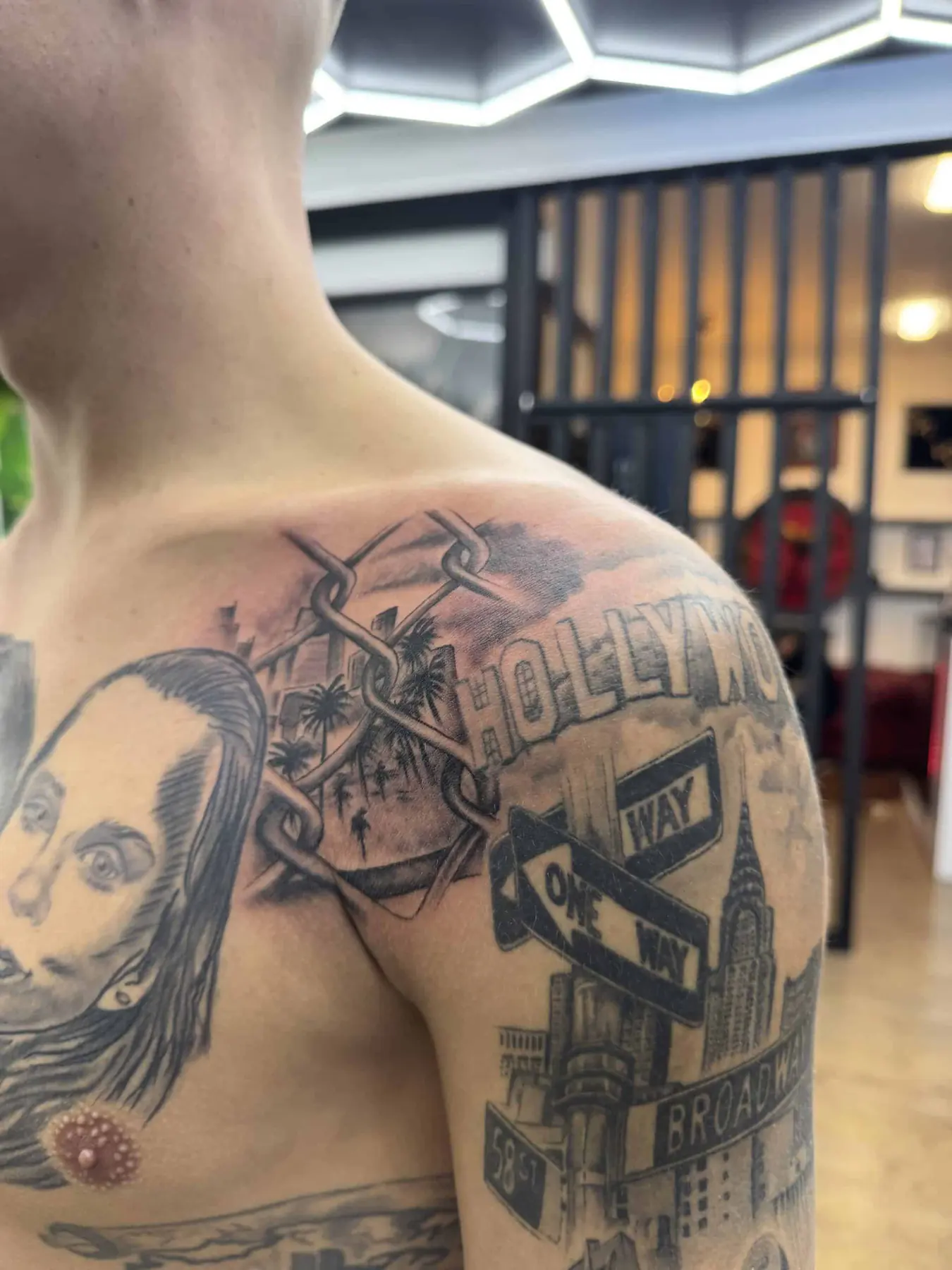 Black and grey collage tattoo on the shoulder: fence with palms, Hollywood sign, street signs and skyline, Vienna