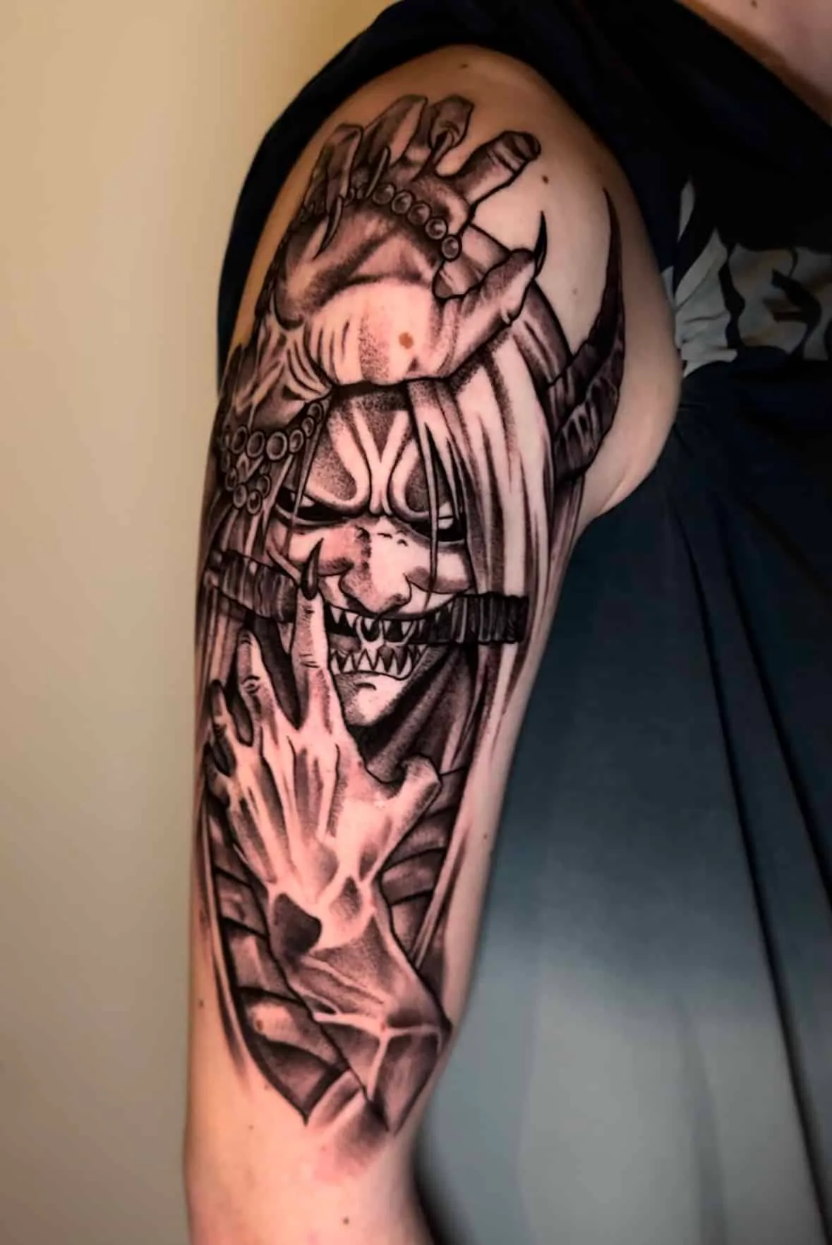 Blackwork tattoo of a horned Japanese oni demon mask with clawed hands on the upper arm, tattoo studio Vienna