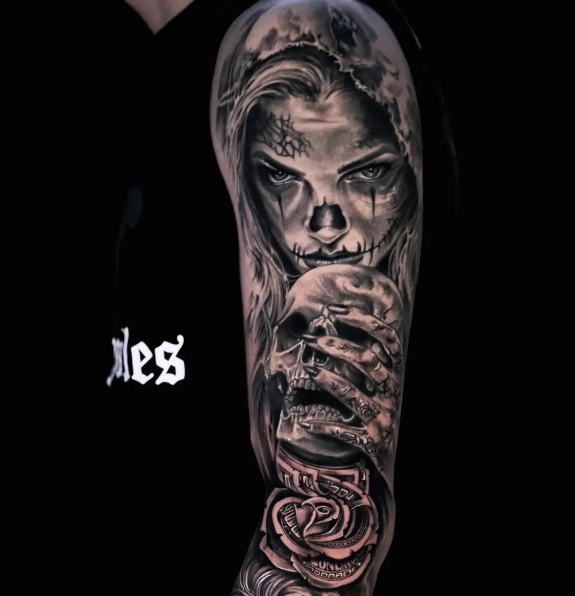 Black and grey arm sleeve: hooded La Catrina with sugar skull make-up, a hand holding a skull and a rose, tattoo Vienna