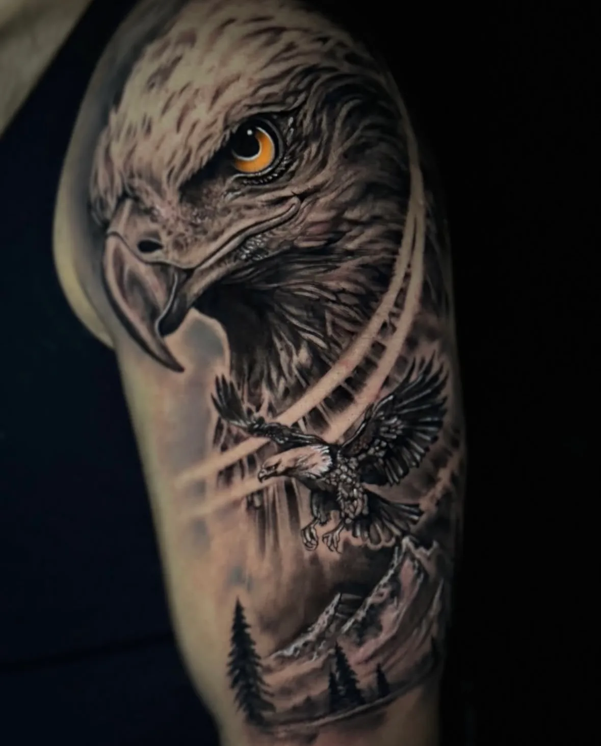 Realistic eagle tattoo on the upper arm: eagle head with an amber eye, an eagle in flight, mountains and pines, Vienna