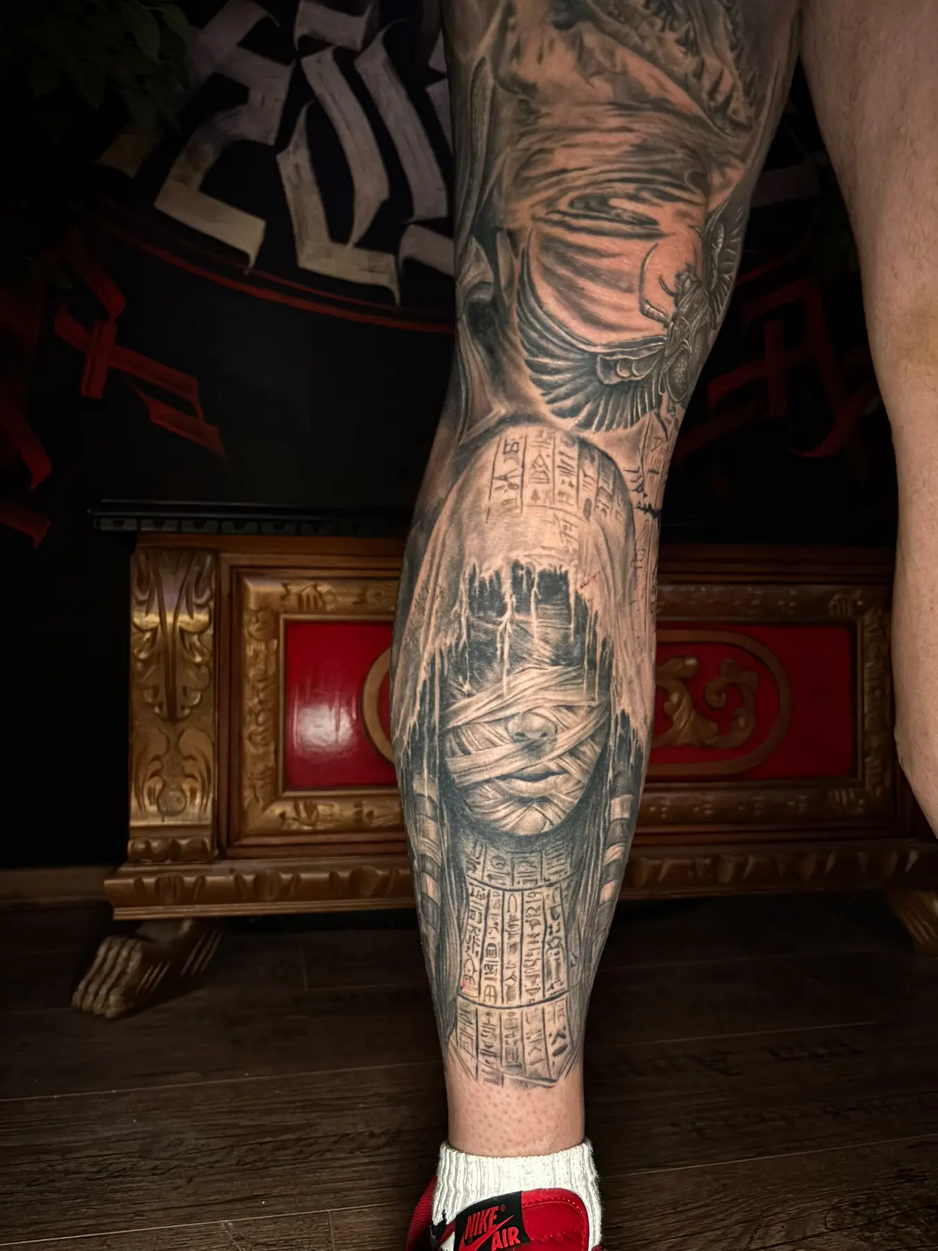 Black and grey calf tattoo: a blindfolded Egyptian woman, hieroglyphs and a winged scarab as part of a leg sleeve