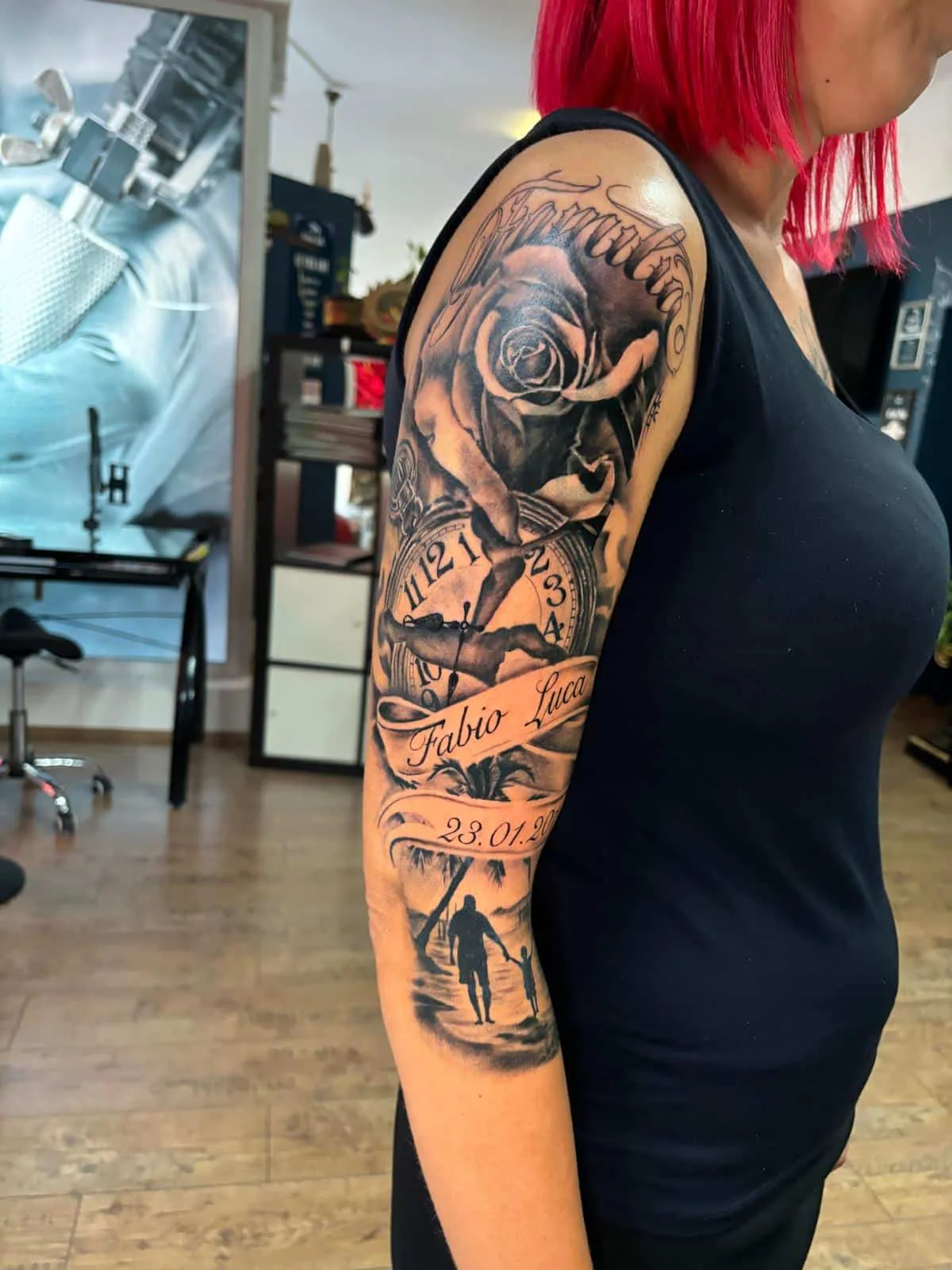 Black and grey half sleeve with a rose, a clock, a name banner and a father-and-child silhouette on a beach, Vienna