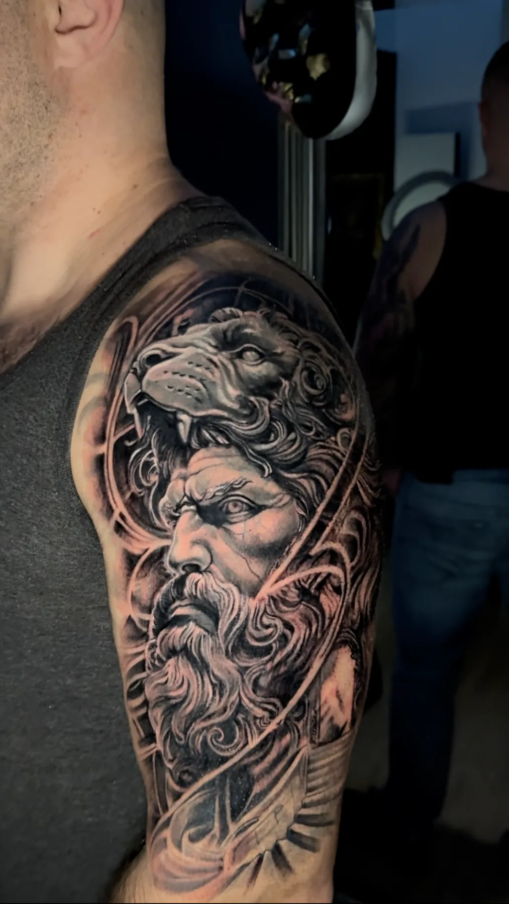 Realistic black and grey tattoo of Hercules wearing the Nemean lion's pelt on the shoulder and upper arm, Vienna