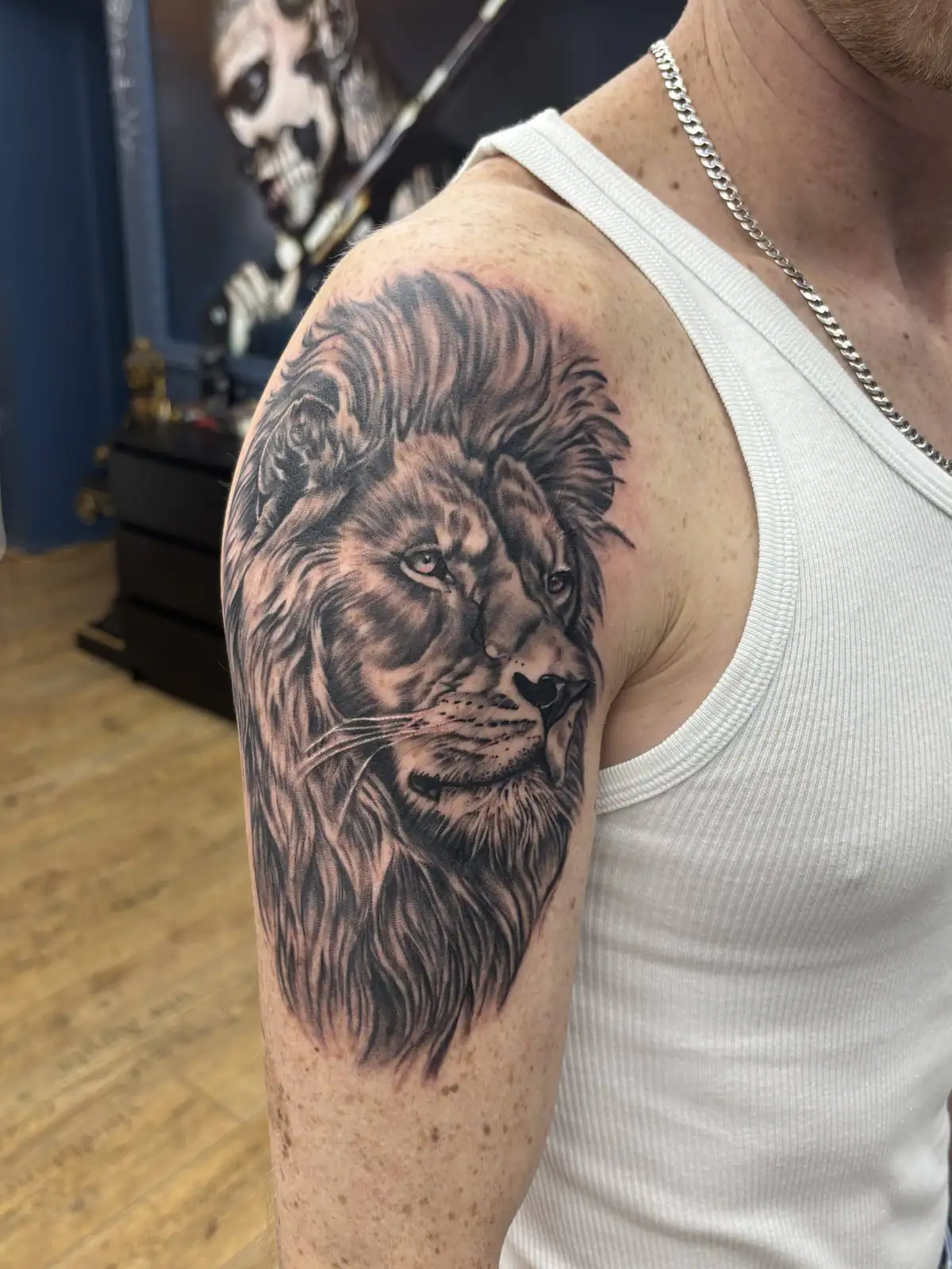 Realistic black and grey lion head tattoo with a full mane on the shoulder and upper arm, photographed at the Vienna studio