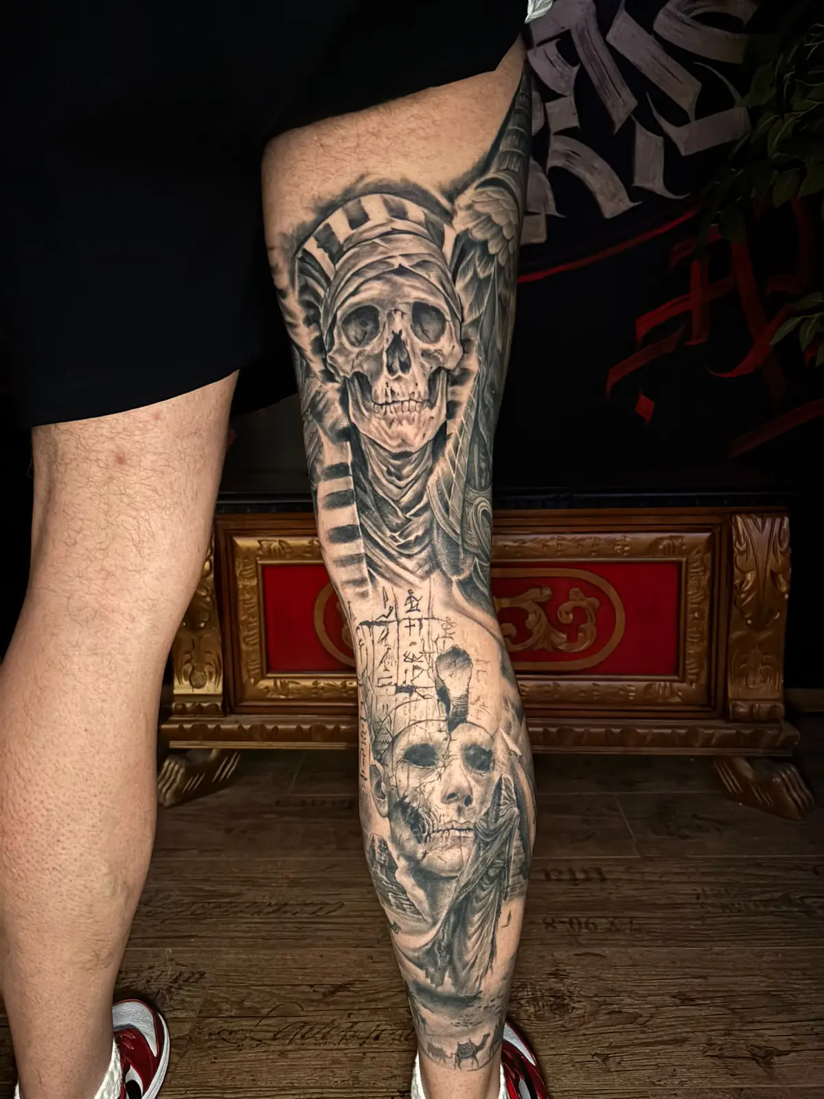 Back of an Egyptian leg sleeve: a skull in a pharaoh's headdress, hieroglyphs and a mummy face in black and grey, Vienna