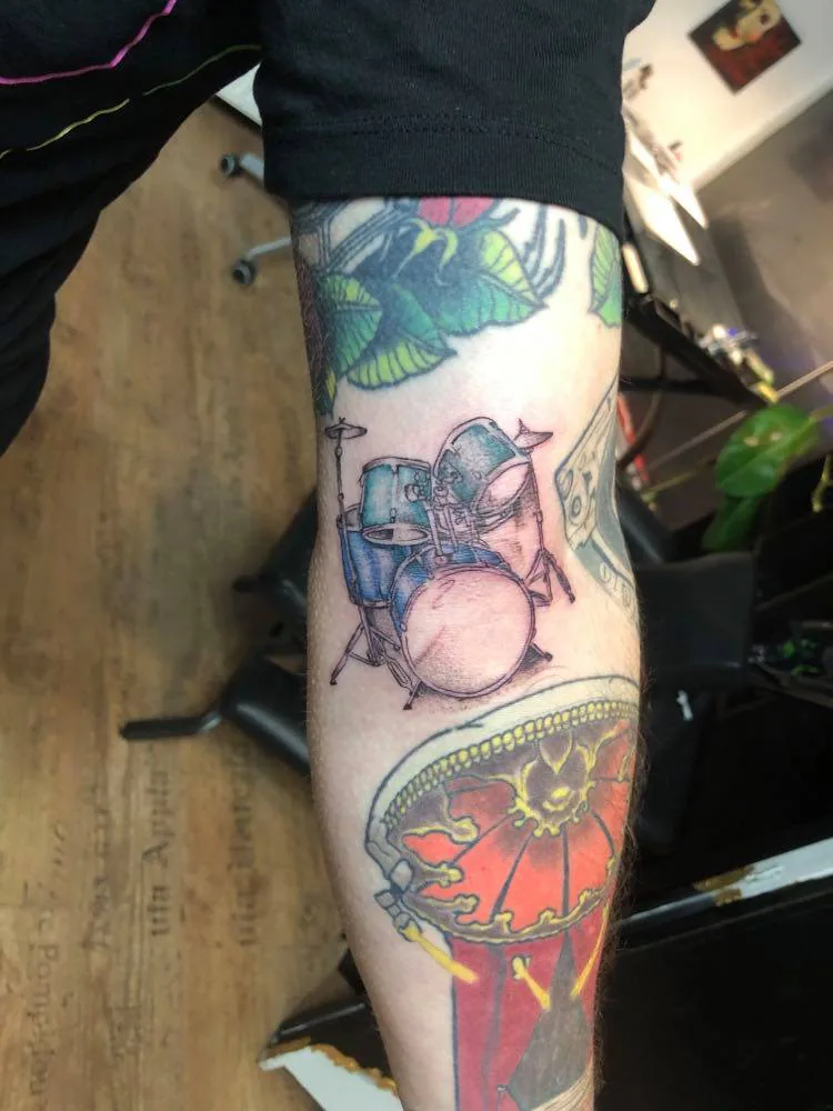 Small drum kit among colour tattoos. Tattoo at Ink21 in Vienna.