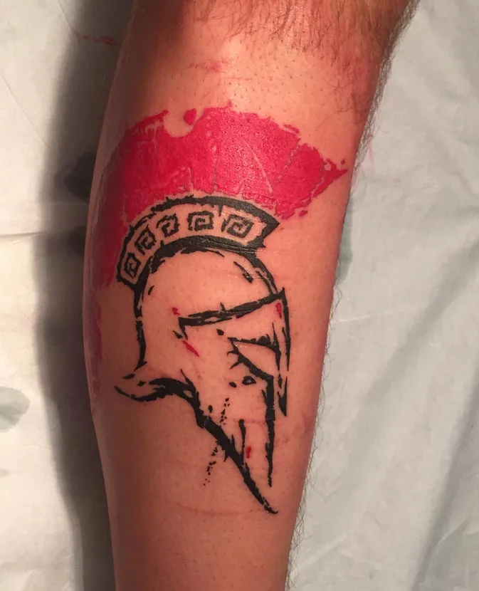 Spartan helmet with a red brush stroke. Tattoo at Ink21 in Vienna.
